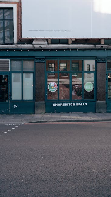 A multi-storey building with large, grid-patterned windows, situated on a city street. The ground floor features a storefront with a black façade displaying the phrase 'SLUSH AGAINST DULL' in bold wh